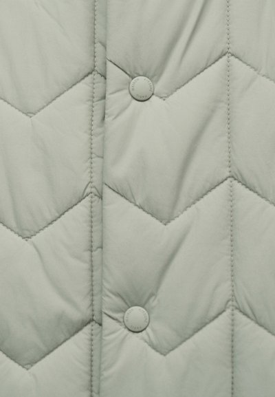 Tissu gris clair matelassé avec couture en chevron et deux boutons-pression ronds étiquetés "Maison Kitsuné Paris."