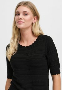 Haut noir texturé à manches courtes, avec un col en dentelle et un design côtelé. Le tissu présente un motif ondulé et une apparence douce.