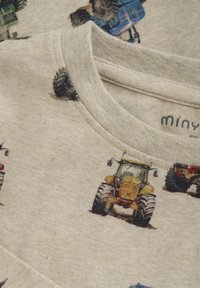 Beige Baumwoll-T-Shirt mit einem wiederholten Traktorprint in verschiedenen Farben. Der Rundhalsausschnitt hat eine angenehme Textur und eine leicht gerippte Oberfläche.