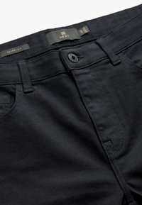 Melni skinny fit džinsi, kas izgatavoti no denima, ar jostu ar pogu, plakanu priekšējo kabatu un tonālām šuvju detaļām.