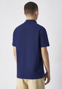 Granatowa koszulka polo z krótkim rękawem, płaskim kołnierzykiem i bocznymi rozporkami u dołu. Wykonana z gładkiego, lekkiego materiału.