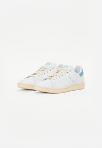 Hvide lædersneakers med lyseblå detaljer, rund tå og beige gummisål. Har perforerede detaljer og flade snørebånd.