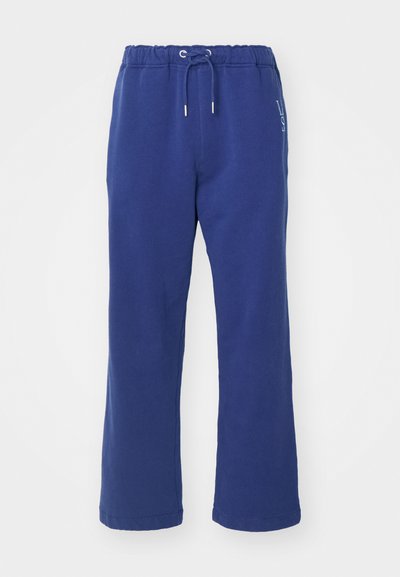 Blauwe trainingsbroek met een drawstring tailleband, losse pasvorm, zachte textuur en witte logodetail aan de zijkant.