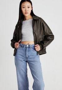 Dark green faux leather jacket with ribbed cuffs, zip closure, and tailored fit, worn over a gray cropped top with light blue high-waisted jeans.