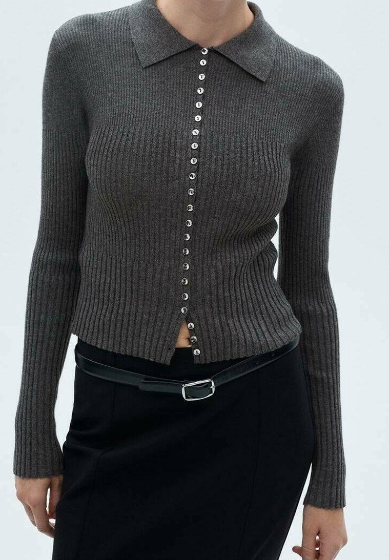 Femme portant un cardigan ajusté en maille côtelée gris foncé boutonné avec col, associé à une jupe noire et une ceinture noire avec une boucle argentée.