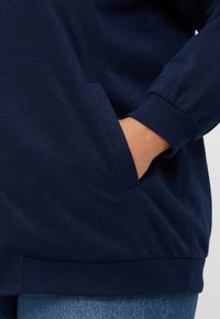 Navy blue sweatshirt with ribbed cuffs and hem, featuring a side pocket. Material appears soft and textured, suitable for casual wear.
