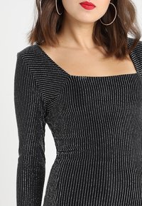 Zwarte jurk met lange mouwen, vierkante halslijn en zilveren verticale strepen, met een aansluitend ontwerp en textuurstof.