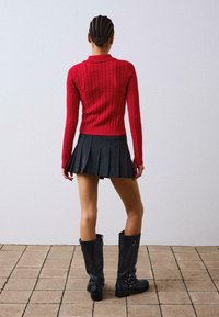 Rdeča pletena jopica z visokim ovratnikom, v kombinaciji s plisirano krilo z pinstripi. Črne škornje do kolen z zaponkami in okroglo konico.