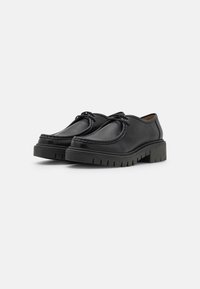 Zwarte leren schoenen met een ronde neus, vetersluitingen en een dikke rubberen zool met een geribbelpatroon voor betere grip.