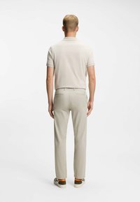 Hellgraues Poloshirt mit kurzen Ärmeln, kombiniert mit beigen Hosen und gemusterten Schuhen mit orangen Akzenten, von hinten gesehen.