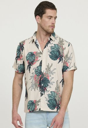 Chemise à manches courtes en beige clair avec un imprimé de feuilles tropicales multicolores. Dotée d'une fermeture à boutons sur le devant et d'une coupe décontractée. Texture de tissu douce.