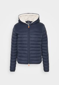 Marineblauwe pufferjack met ritssluiting aan de voorkant, capuchon en crèmekleurige voering. Heeft gestikte horizontale secties en een oranje ritssluiting trekker.