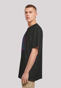 Svart oversized t-skjorte med et fargerikt geometrisk grafisk design foran. Korte ermer, rund hals og laget av bomull.