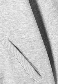 Szürke kapucnis pulóver anyag sima textúrával. Oldalzseb bordázott díszítéssel. Egyszerű, mintázat nélküli kialakítás. Puha és kényelmes anyag.