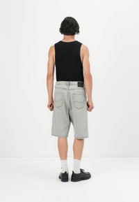 Grå denimshorts med en afslappet pasform, skåret over knæet, og en sort ribbet tanktop. Indeholder baglommer og et mærke i sort læder på taljebåndet.