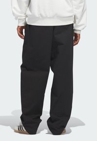 Μαύρο παντελόνι με φαρδύ πόδι από λείο ύφασμα, με πλαϊνές τσέπες και άνετη εφαρμογή, συνδυασμένο με άσπρα και μαύρα αθλητικά παπούτσια.