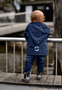 Tummansininen vedenpitävä huppari, jossa "RECYCLED"-logo. Yhdistetty tummansinisiin farkkuihin ja tyylikkäisiin keltaisiin sadekengän saappaisiin.