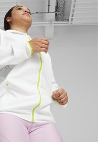 Vit zip-up jacka med neongröna accenter, med en hög krage och ett texturerat mönster på ärmarna. Tillsammans med ljuslila leggings.