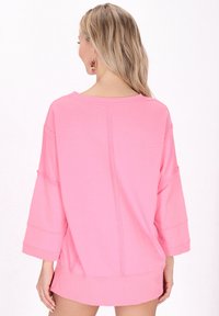 Vaaleanpunainen ylisuuri collegepaita, jossa on rento istuvuus, leveät hihat ja ompeluyksityiskohtia. Pehmeä pinta, pyöreä pääntie ja helma ulottuu lantioon.