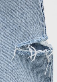 Jean en denim bleu clair avec un ourlet effiloché. Le tissu présente un motif classique en sergé et un léger délavage, laissant apparaître les bords bruts au niveau de l'ourlet.