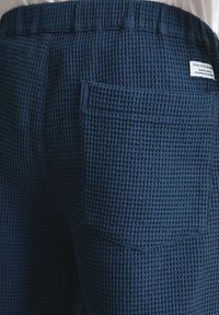 Marineblauwe broek gemaakt van gestructureerde, wafelpatroonstof. Heeft een elastische tailleband en een achterzak.