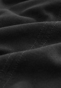 Tissu noir à surface douce et texturée, présentant des motifs de couture subtils en gris clair. Des plis lisses créent une impression de profondeur.