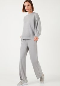 Sudadera gris clara con cuello redondo y mangas largas, combinada con pantalones gris claros a juego. Textura suave, corte relajado, diseño minimalista.