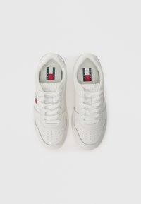 Baskets en cuir blanc avec un bout perforé, des lacets plats et un logo rouge et bleu sur le côté. Semelle en caoutchouc et col rembourré pour le confort.