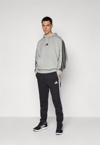 Gray hoodie with black stripes, logo on chest; paired with black sweatpants featuring white stripes and logo; black athletic shoes.