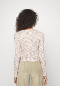 Camisa cropped de mangas longas em um tecido texturizado com um padrão multicolorido nas tonalidades de rosa, branco e cinza. Decote arredondado, design ajustado.
