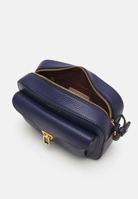 Dunkelblaue Leder-Crossbody-Tasche mit goldfarbenem Reißverschluss und Verschluss, mit einer Vordertasche und verstellbarem Tragegurt auf einem weißen Hintergrund.