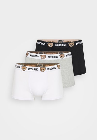 Três pares de boxers: branco, cinza e preto. Cada um tem uma faixa com um design de urso de pelúcia e a marca "Moschino".