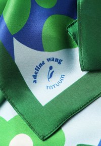 Foulard din mătase verde și albastră cu un model geometric ce include forme rotunjite; conține un logo cu textul: "adeline wang" și "TNTUUM." Marginile sunt cusute.