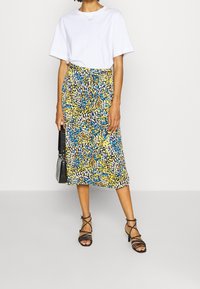 Falda midi con estampado floral en azul, amarillo y negro, combinada con una camiseta blanca. Presenta una cinturilla elástica y un ajuste holgado.