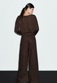 Bruine geribde gebreide trui met een wijd decolleté, gecombineerd met bruin hoge taille wijde broek met een achterzak.