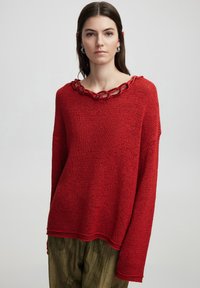 Roter gestrickter Pullover mit lockerer Passform, aus strukturiertem Stoff und einem markanten Kettenhals. Lange Ärmel, abgerundeter Saum.