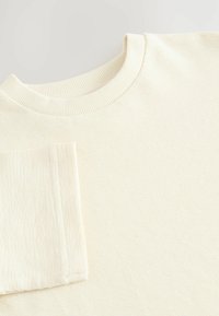 Cremefarvet ribbesweater med rund halsudskæring og korte ærmer. Stoffet har et struktureret mønster og en glat finish.
