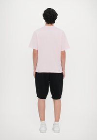Helles rosa Baumwoll-T-Shirt mit kurzen Ärmeln und Rundhalsausschnitt, kombiniert mit schwarzen knielangen Shorts, getragen mit weißen Sneakers.