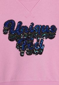 Ροζ φούτερ με V-λαιμόκοψη. Περιλαμβάνει ένα σχέδιο "Unique Feel" με παγιέτες σε σκοτεινό μπλε, πράσινο και μαύρο. Μαλακή υφή, χαλαρός στυλ.