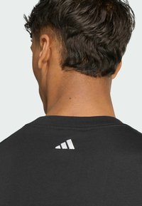 Sort t-shirt med rund hals, med et hvidt Adidas-logo på ryggen. Glat tekstur og korte ærmer.