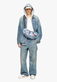 Giacca in denim e jeans di blu chiaro, felpa con cappuccio, t-shirt bianca e borsa a tracolla con fantasia. Sneaker con dettagli rossi.