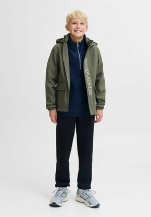 Grön vattentät jacka med logotyp, marinblå stickad tröja, svarta byxor och grå sneakers. Har huva och framfickor.