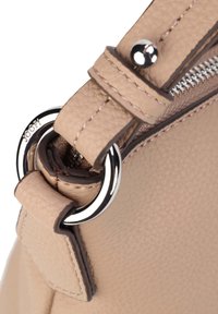 Roh béžové texturované kožené tašky se stříbrným kovovým kroužkem a zipem, s názvem značky vyraženým na kroužku.