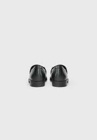 Sapatos de couro pretos com bico arredondado, apresentando um salto baixo e um design simples. Textura lisa com detalhes mínimos e sem acentos visíveis.