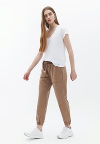 T-shirt bianco a maniche corte con scollo a V abbinato a pantaloni jogger marroni con coulisse e scarpe da ginnastica bianche, con polsini elastici e tasche laterali.