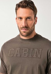 Olivengrøn t-shirt med rund hals i blødt stof med hævet "CABIN"-bogstaver i mørkere tråd på brystet. Almindelig pasform, korte ærmer.