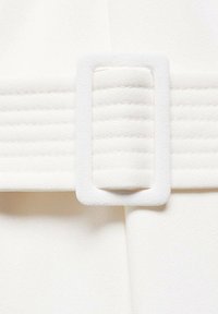 Gros plan d'une ceinture en tissu blanc avec une boucle rectangulaire et des lignes horizontales cousues sur la sangle de la ceinture.