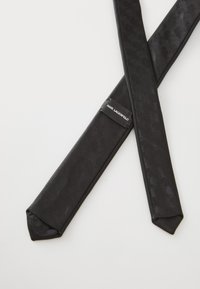 Schleife in Schwarz mit strukturiertem Muster, mit spitzem Ende. Enthält ein Etikett mit "KARL LAGERFELD" auf einem Band zur sicheren Anpassung.