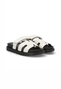 Sandalias deslizantes en blanco y negro que presentan un diseño de tira ancha, una suela texturizada y una estética minimalista con bandas entrelazadas.
