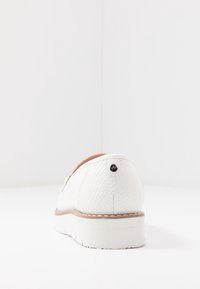 Vita slip-on sko med strukturerat reptilmönster, rundad baksida och en ljusfärgad sula. Har en liten svart logotypdetalj vid hälen.